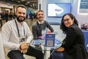 Registro do evento Conarec 2022. Na foto, três pessoas, sendo dois homens e uma mulher, sentados, olhando pra frente e sorrindo. Eles vestem roupas sociais e estão no stand da Algar Tech.