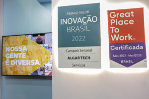 Registro do evento Conarec 2022. Foto de uma parede do stand. Na parede tem uma TV com a imagem: Nossa gente é diversa. Ao lado têm emblemas do: Prêmio Valor Inovação Brasil 2022 e do Great Place To Work - Certificada