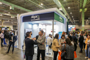 Registro do evento Conarec 2022. Foto ambiente do Stand da Algar Tech. Algumas pessoas foram captadas na imagem transitando ou paradas conversando umas com as outras, ao longe.